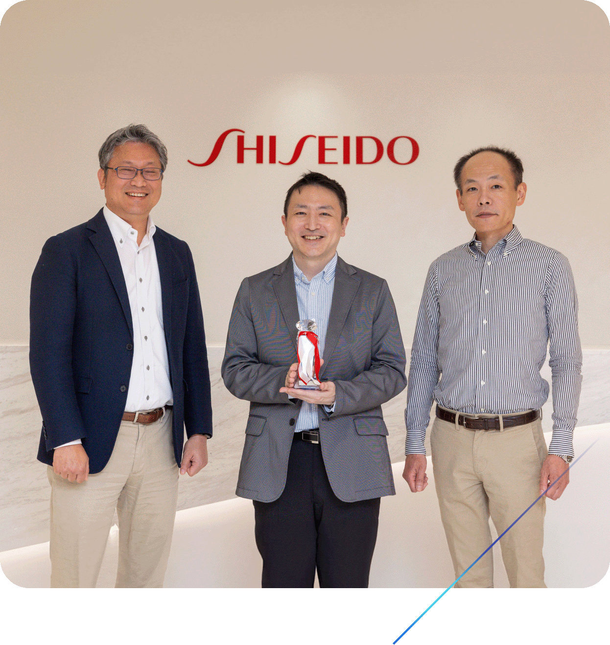 Three Shiseido team members standing in front of a Shiseido logo, holding an award