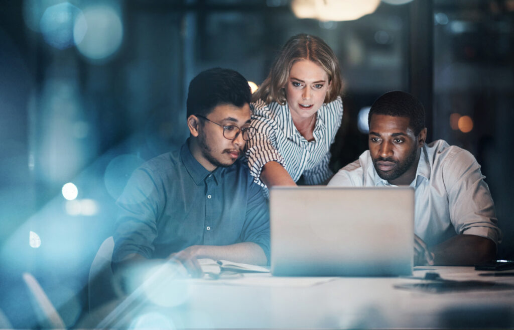 Three colleagues reviewing a laptop screen together in an office environment.